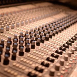 Detailed view of an analog audio mixing console with various knobs and sliders in a sound studio.