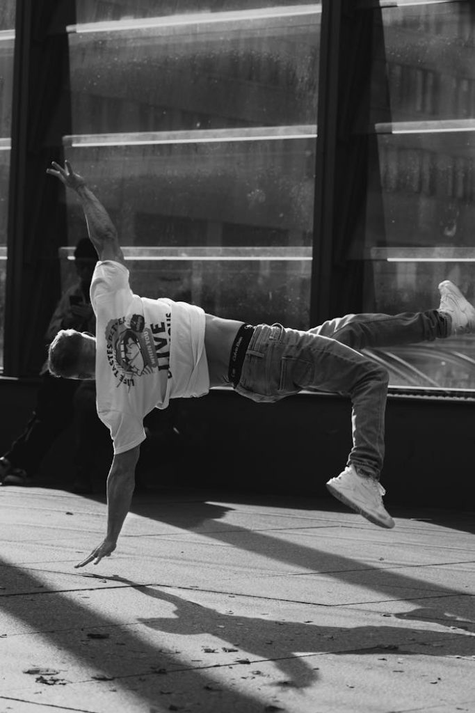 Black and white photo of a man breakdancing on an urban sidewalk, showcasing movement and creativity.